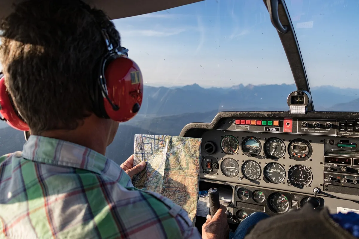 Dans un DR400 en vol au-dessus des Alpes, le pilote relit sa carte aéronautique, une main sur le manche. Photo : Pierre Goiffon, CC BY-SA 4.0