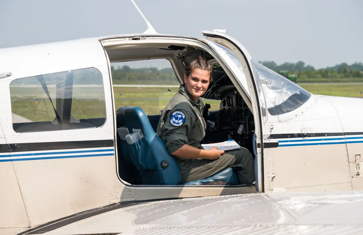 Pendant un stage d'été de pilotage aux États-Unis, une lycéenne en combinaison de vol, check-list en main, assise à la porte d'un avion léger. Photo : US Air Force, domaine public