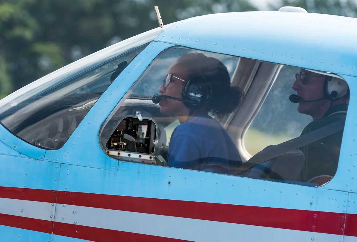 Casque sur les oreilles, une lycéenne s'apprête à rouler vers la piste aux commandes d'un avion léger, son instructeur assis à côté d'elle. Photo : US Air Force, domaine public