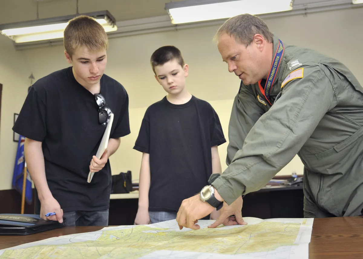 Sur une base aérienne au Japon, un instructeur montre une route sur une carte aéronautique à deux jeunes cadets, carnet en main. Photo : US Air Force, domaine public