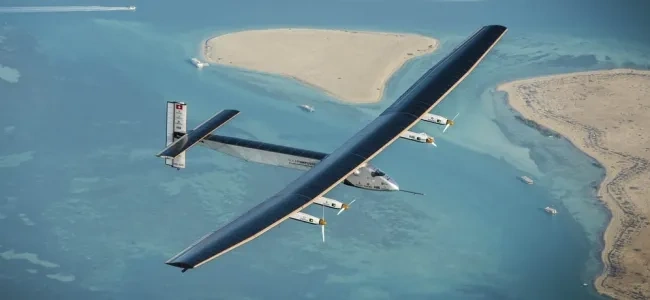 Photographie d’un avion solaire aux très longues ailes, en vol au-dessus de la mer et de bancs de sable